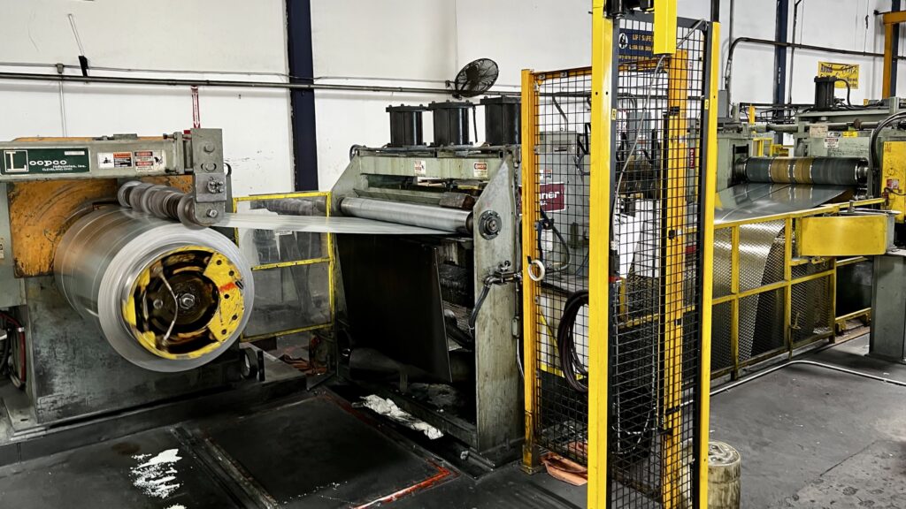 A coil slitting line converts wide mill-produced steel coils into narrower widths used for cold-formed steel framing products. After passing through rotary cutting dies, the slit steel temporarily accumulates in a deep looping pit before being wound into individual slit coils.