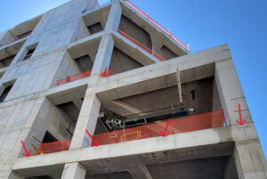 Embedded curtain wall anchorage rails (red arrows) were already cast into the post-tensioned concrete structure before ICS joined the project. Engineers designed the framing around the existing rails because post-installed anchorage was prohibited.