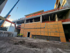 A prefabricated curtain wall panel is hoisted into place. Panel sizes and detailing varied to accommodate as-built structural conditions across the façade.